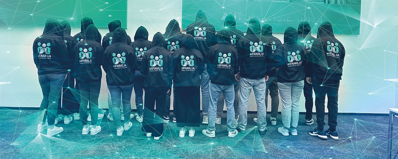 Mehrere Personen stehen nebeneinander mit dem Rücken zur Kamera, tragen schwarze Hoodies mit dem Schriftzug „elFAMILIA“. Die Kapuzen sind aufgesetzt, der Hintergrund ist ein Raum mit digital wirkender, grün-blauer Grafiküberlagerung.