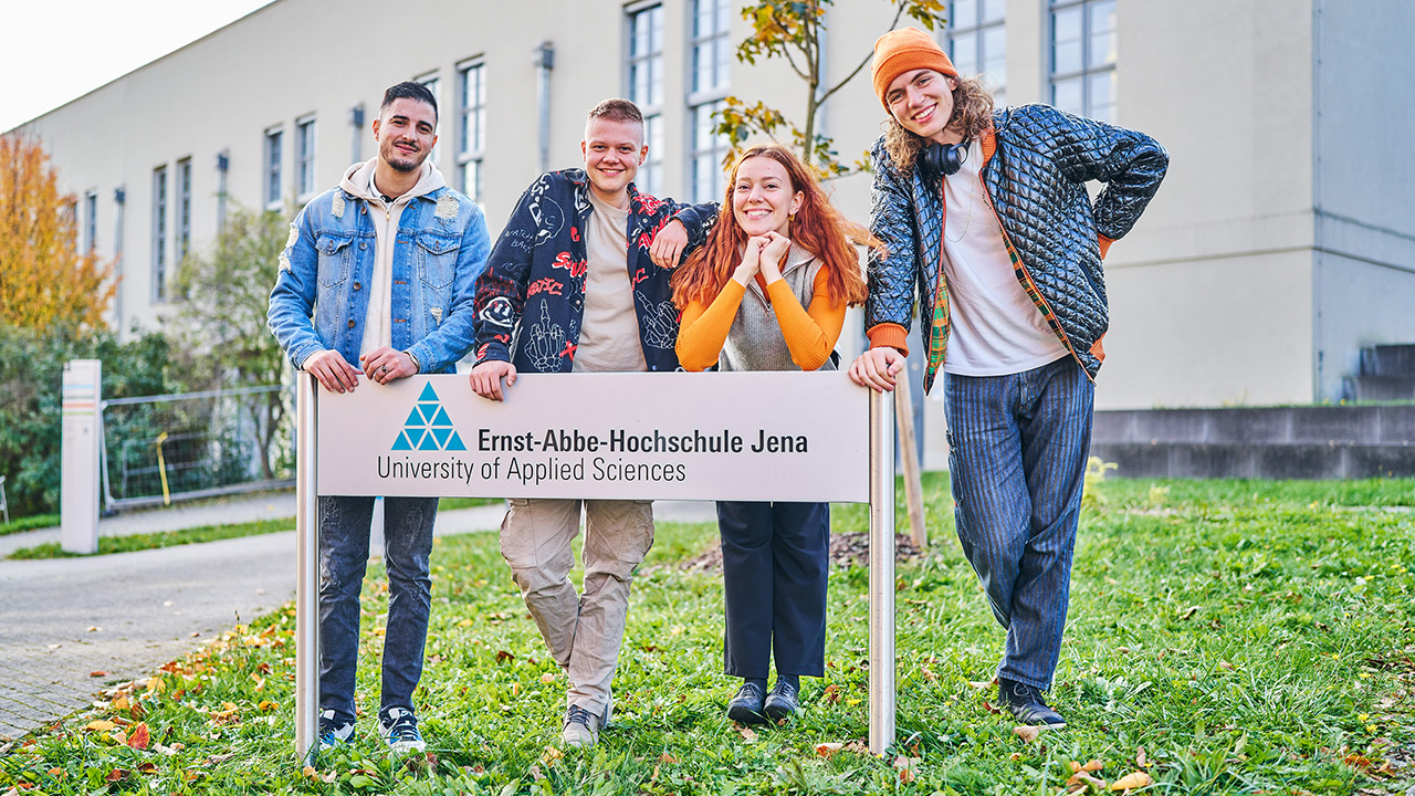 Vier Menschen lehnen auf dem Hochschuleschild