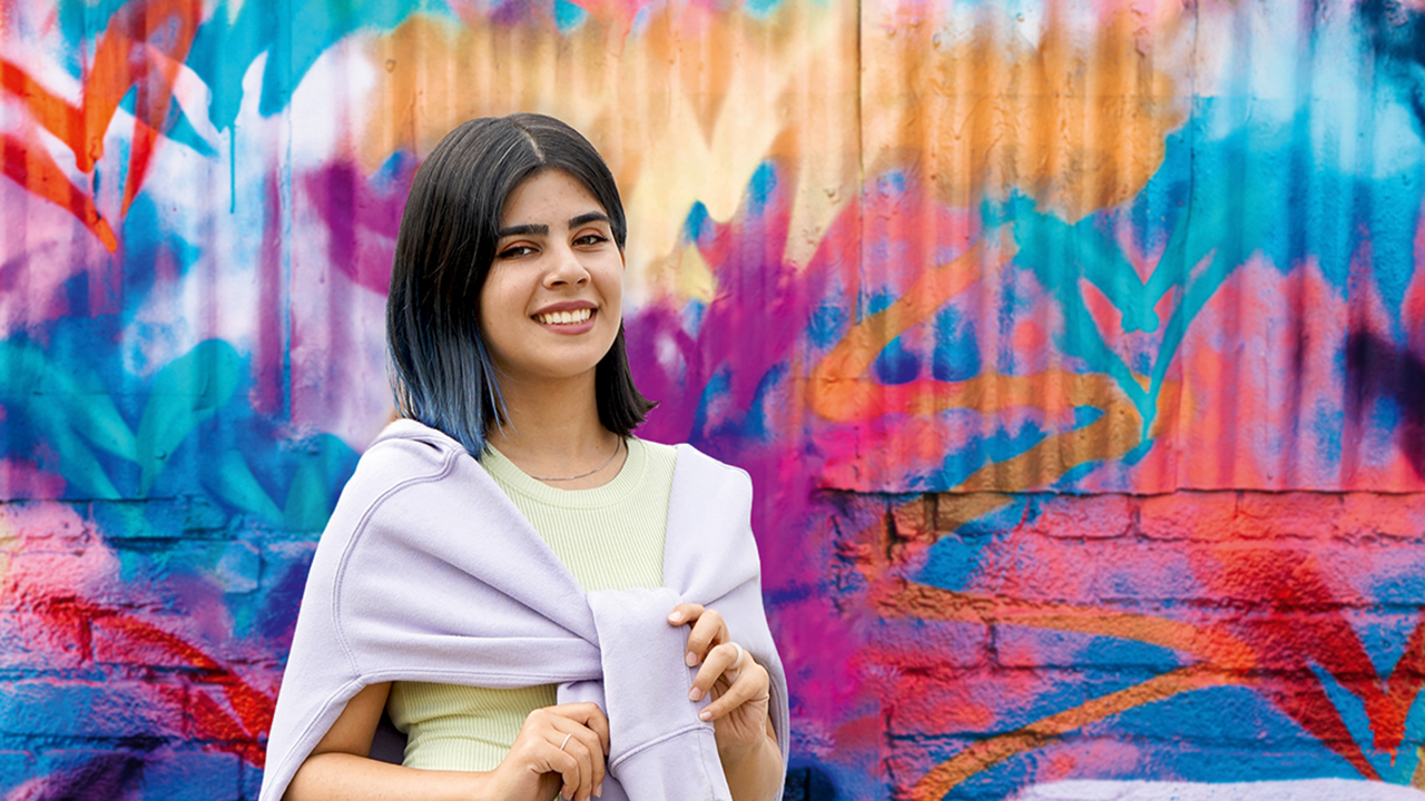 Junge lächelnde Person vor einer mit Graffiti besprühten Wand