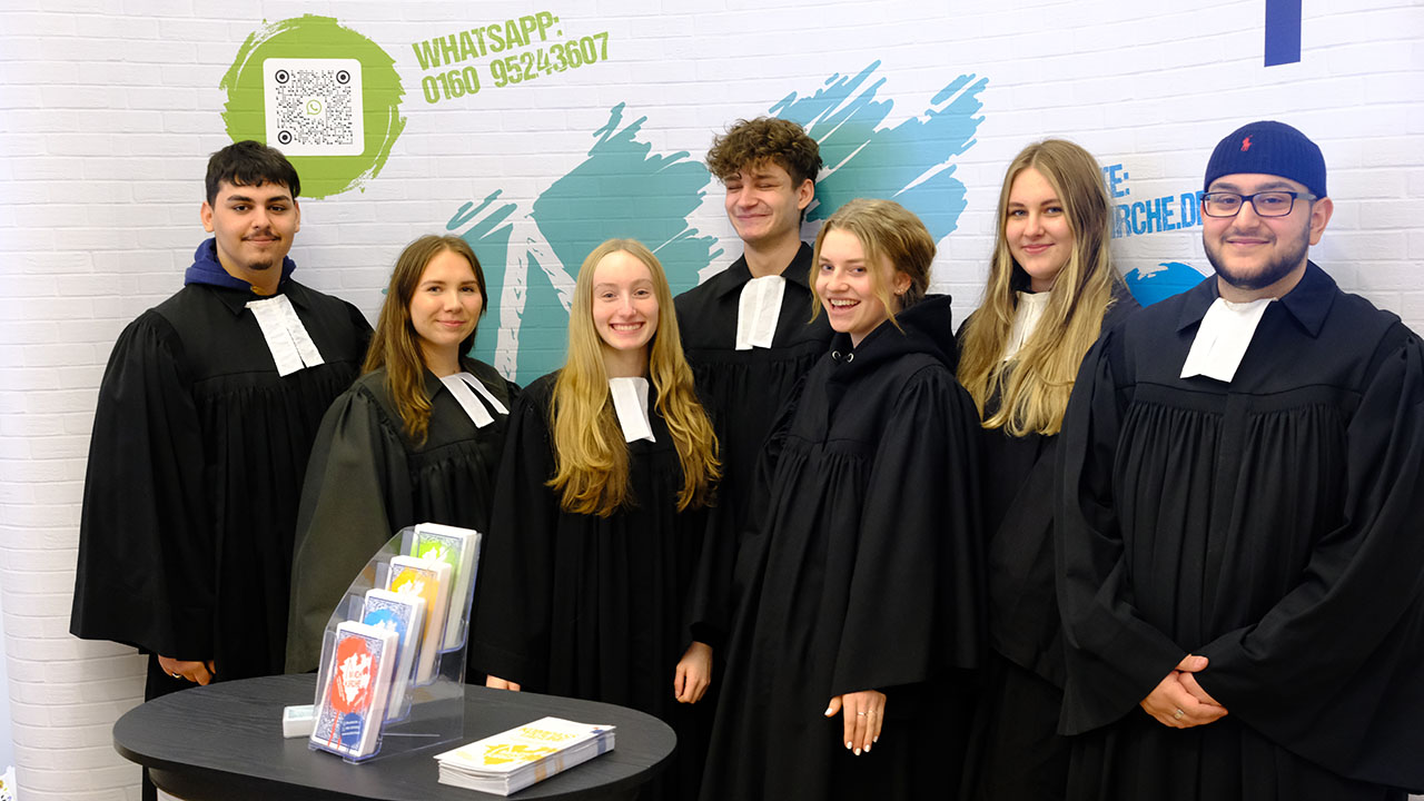 Gruppe junger Personen lächelt in die Kamera und trägt die Robe evangelischer Pfarrer.