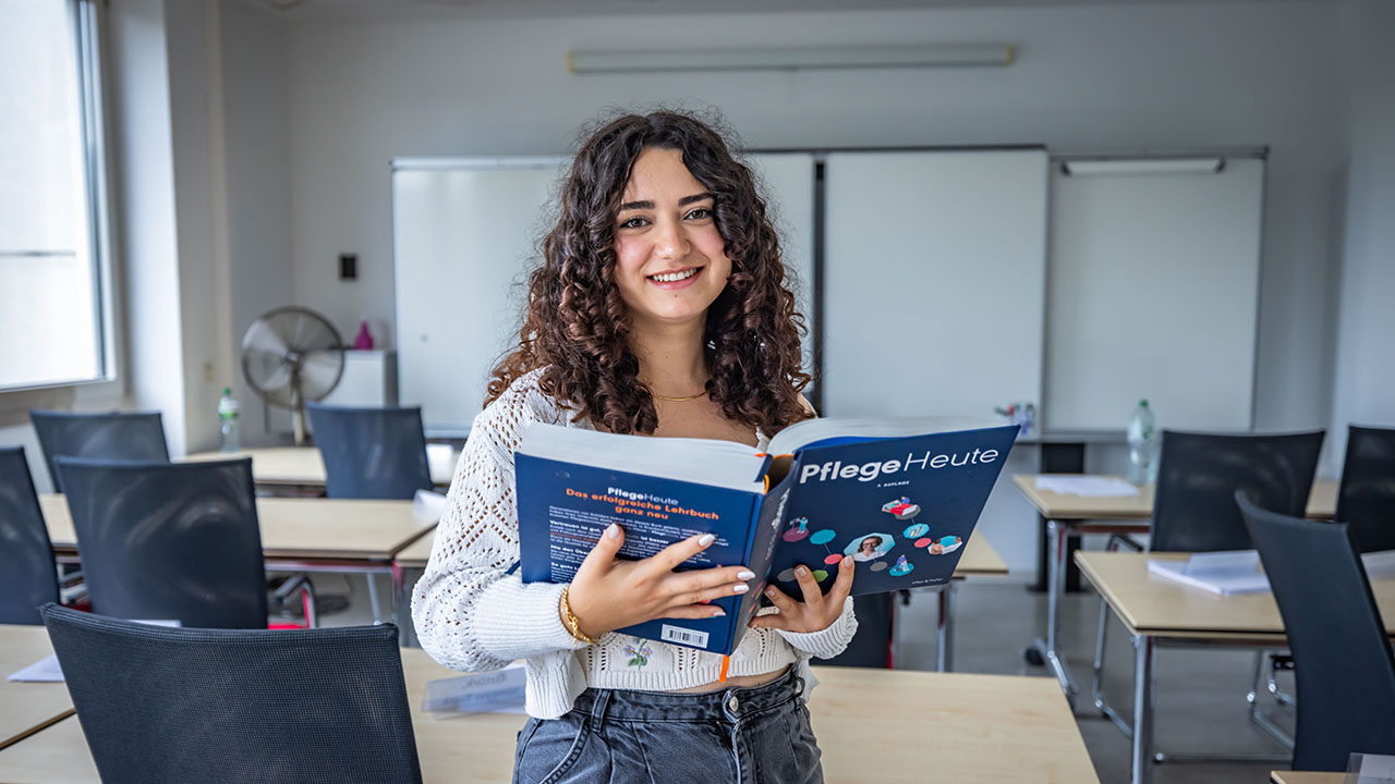 Das bild zeigt eine Persone mit einem großen Pflegebuch in einem Klassenzimmer.