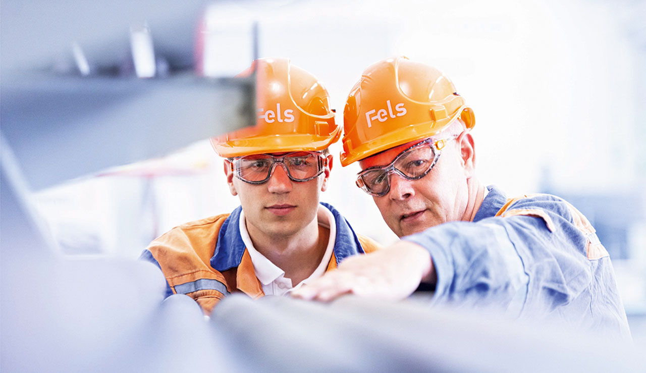 Zwei Männer mit orangen Helmen mit Aufschrift Fels im Gespräch