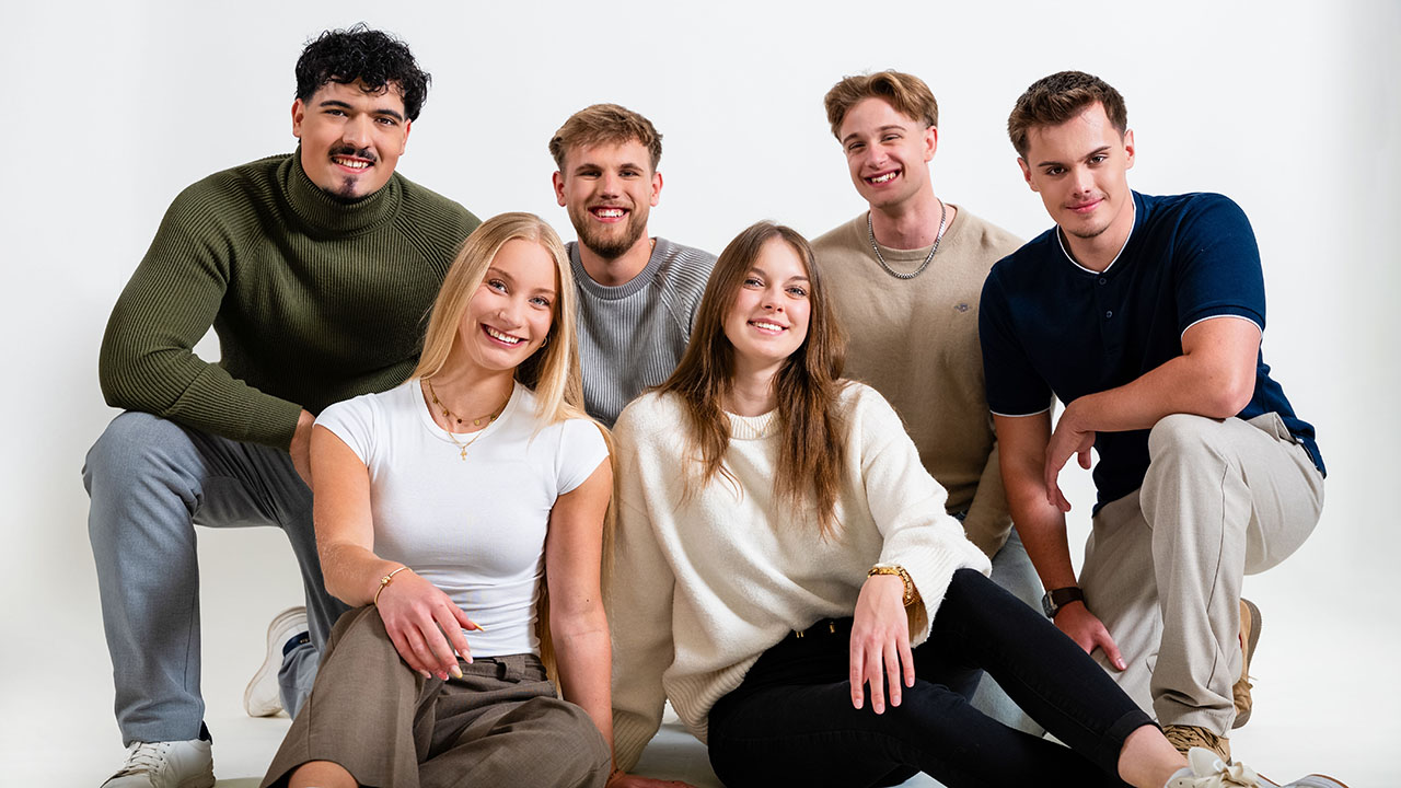 Gruppenfoto mit sechs jungen Personen, die in die Kamera lächeln