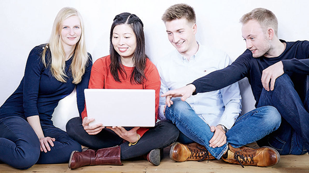 Vier Menschen sitzen auf dem Boden und schauen gemeinsam in einen Laptop