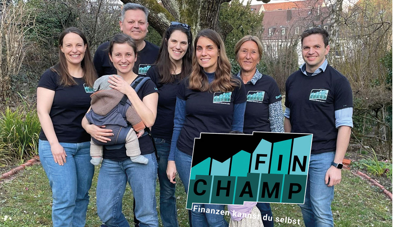 Sieben Personen in dunklen T-Shirts mit dem Logo von FinChamp stehen draußen vor einem Baum und blicken lächelnd in die Kamera.