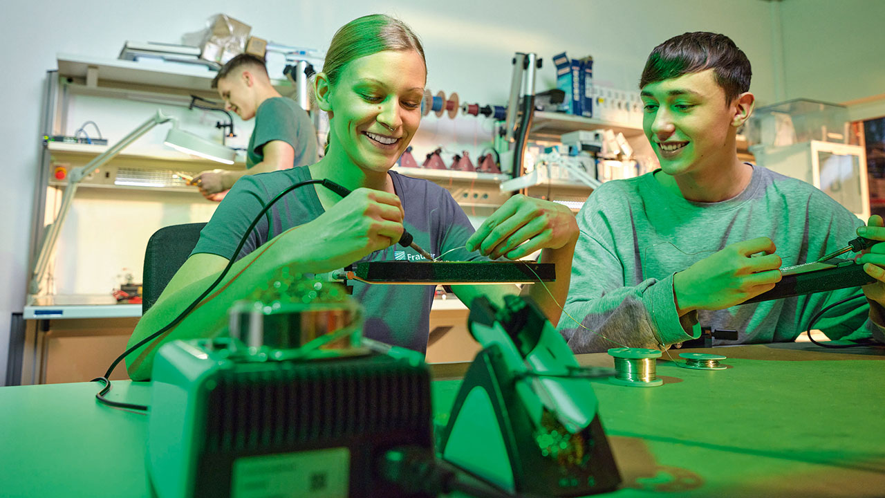 Zwei junge lächelnde Personen arbeiten mit einem Lötkolben