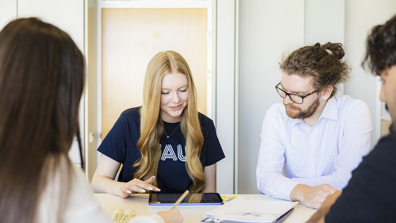 Vier Personen, zwei davon frontal, die auf ein Tablet sehen.