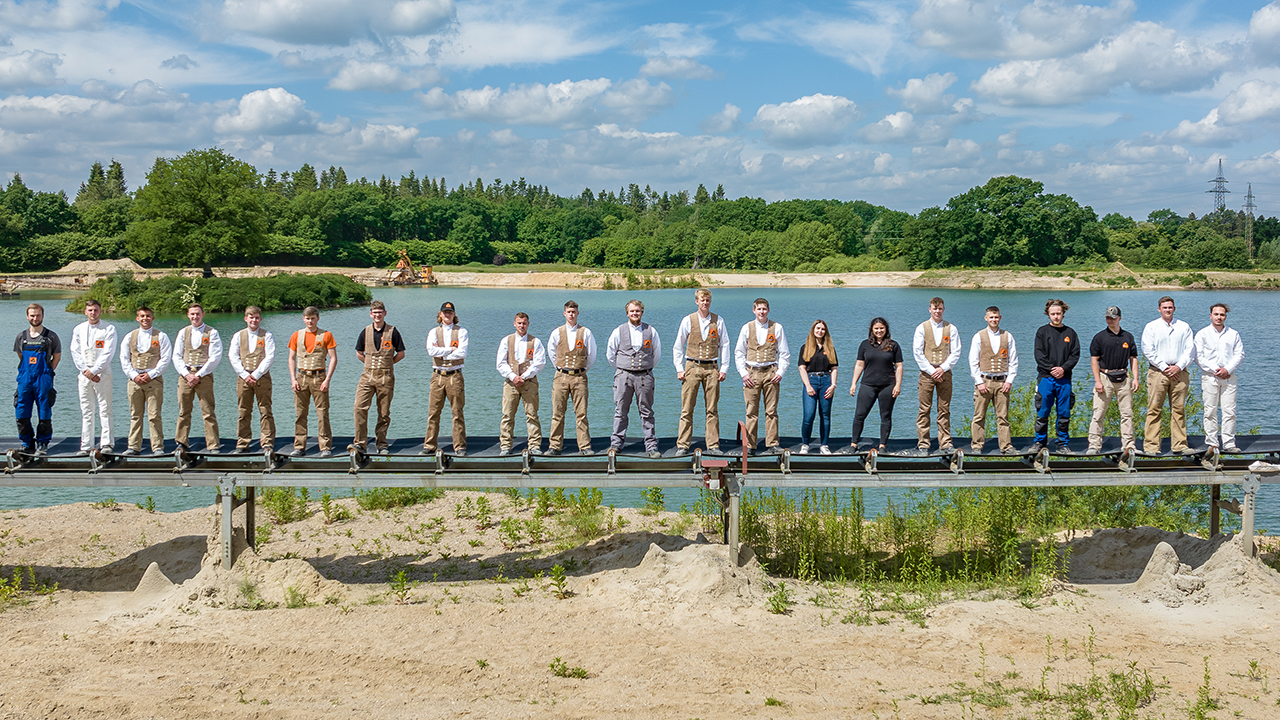 Mitarbeiter stehen aufgereiht nebeneinander vor einem See