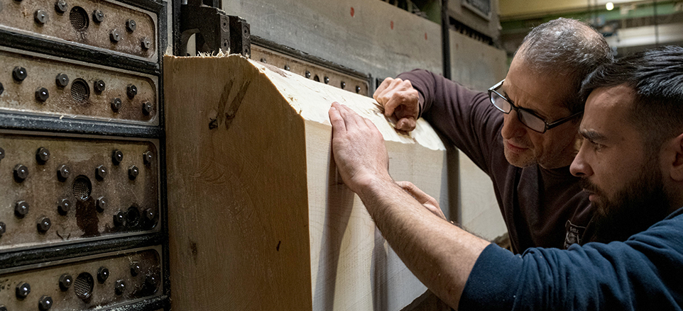 Zwei Mitarbeitende prüfen einen Holzbalken. 