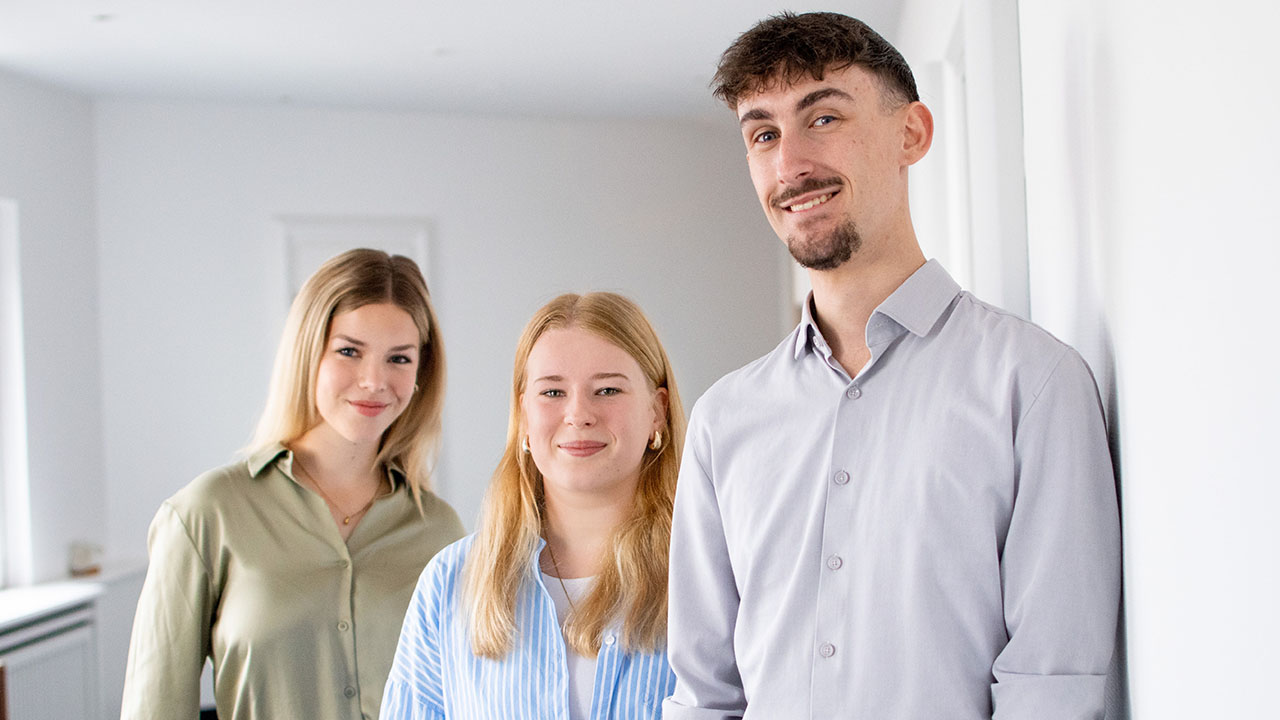 Drei junge Personen lächeln in die Kamera