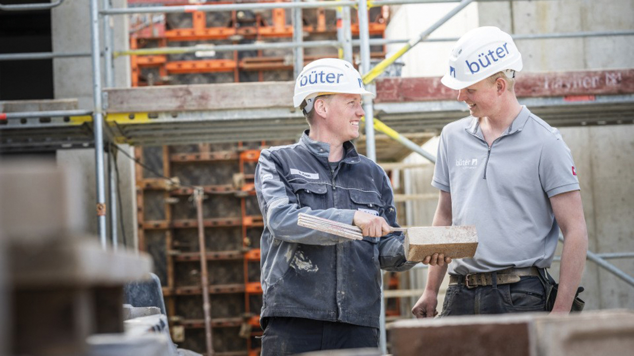 Zwei Personen mit Arbeitshelmen bei einer Baubesprechung, auf den Helmen steht "büter"