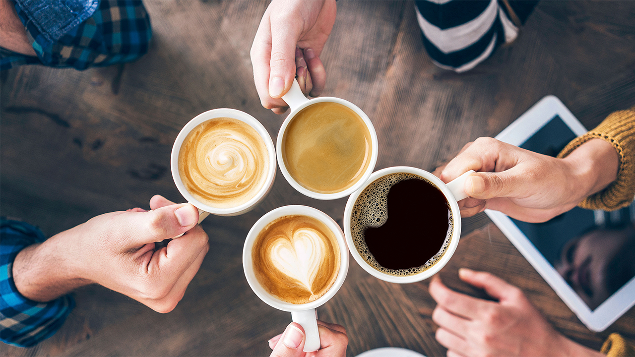 Vier Kaffetassen werden gehalten. Es sind verschieden Kaffeezubereitungen