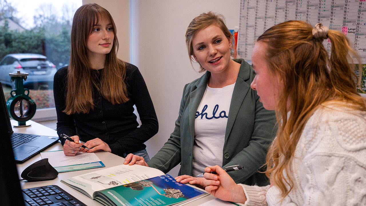 Drei junge Personen im Gespräch am Schreibtisch