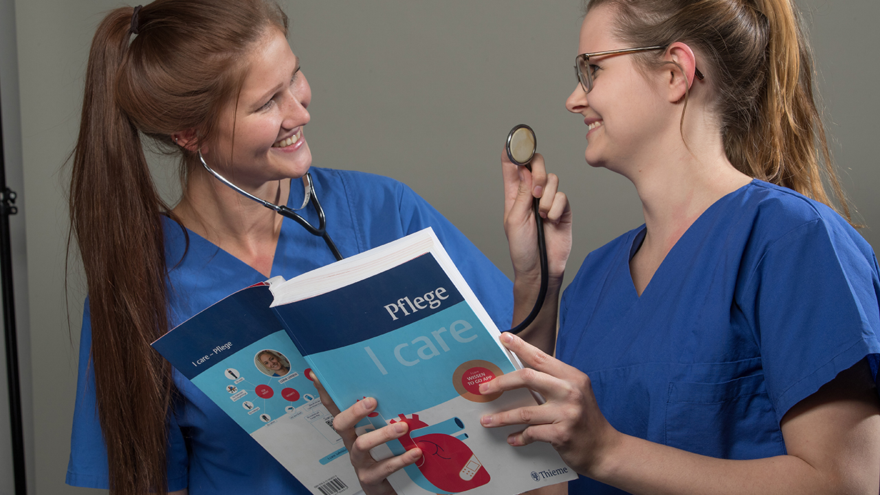 Zwei Mitarbeitende in Krankenschwesterkleidung lächeln sich an