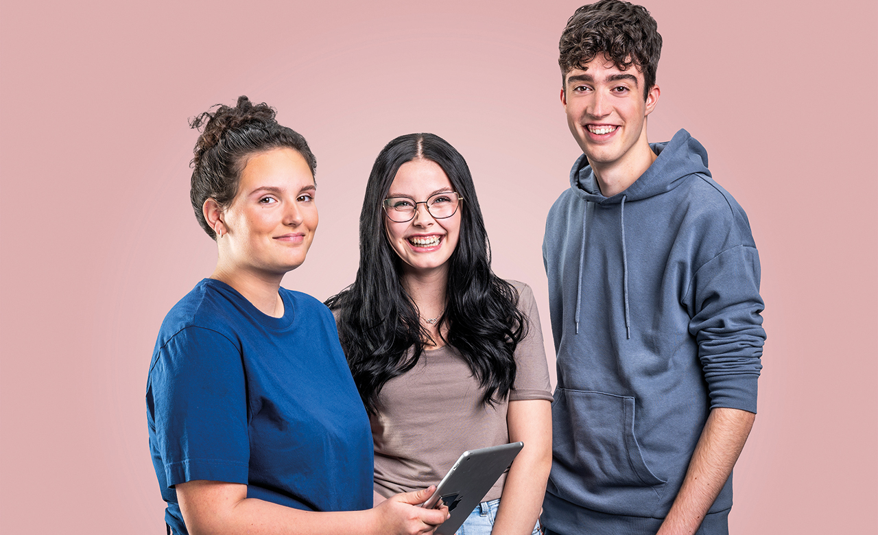 Drei junge Personen vor einem rosa-farbenen Hintergrund lächeln in die Kamera