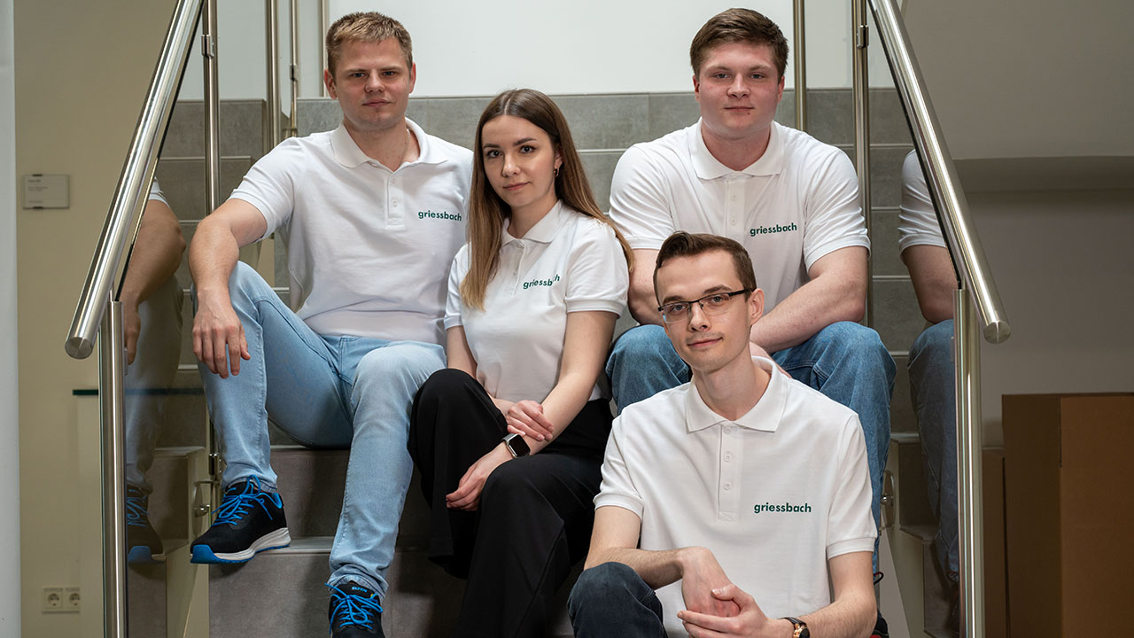 Vier junge Menschen in weißen Polsohirts mit Firmenlogo sitzen auf einer Treppe