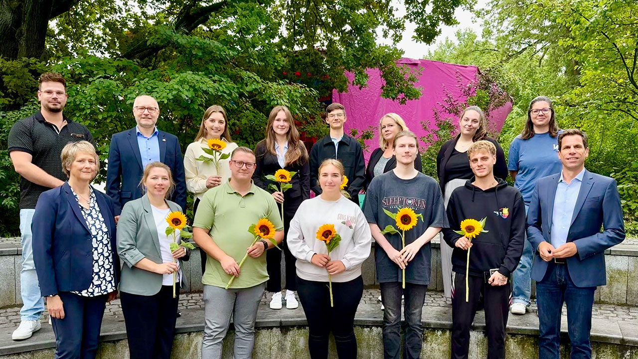 Gruppenfoto im Grünen, Auszubildende halten eine Sonnenblume in der Hand