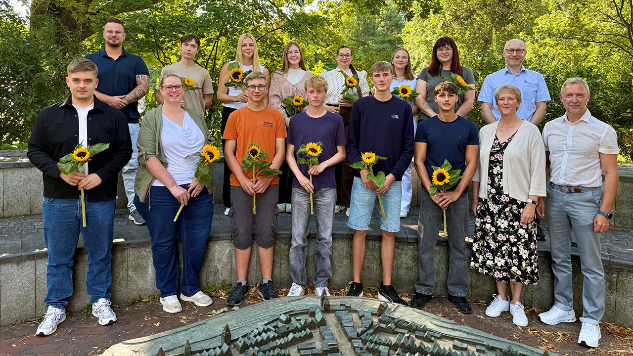 Gruppenfoto im Grünen, Auszubildende halten eine Sonnenblume in der Hand