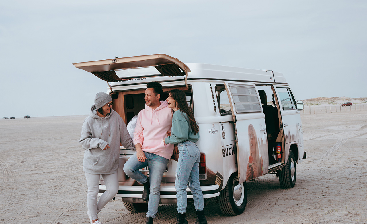 3 Personen am Strand vor einem Camper-Bus