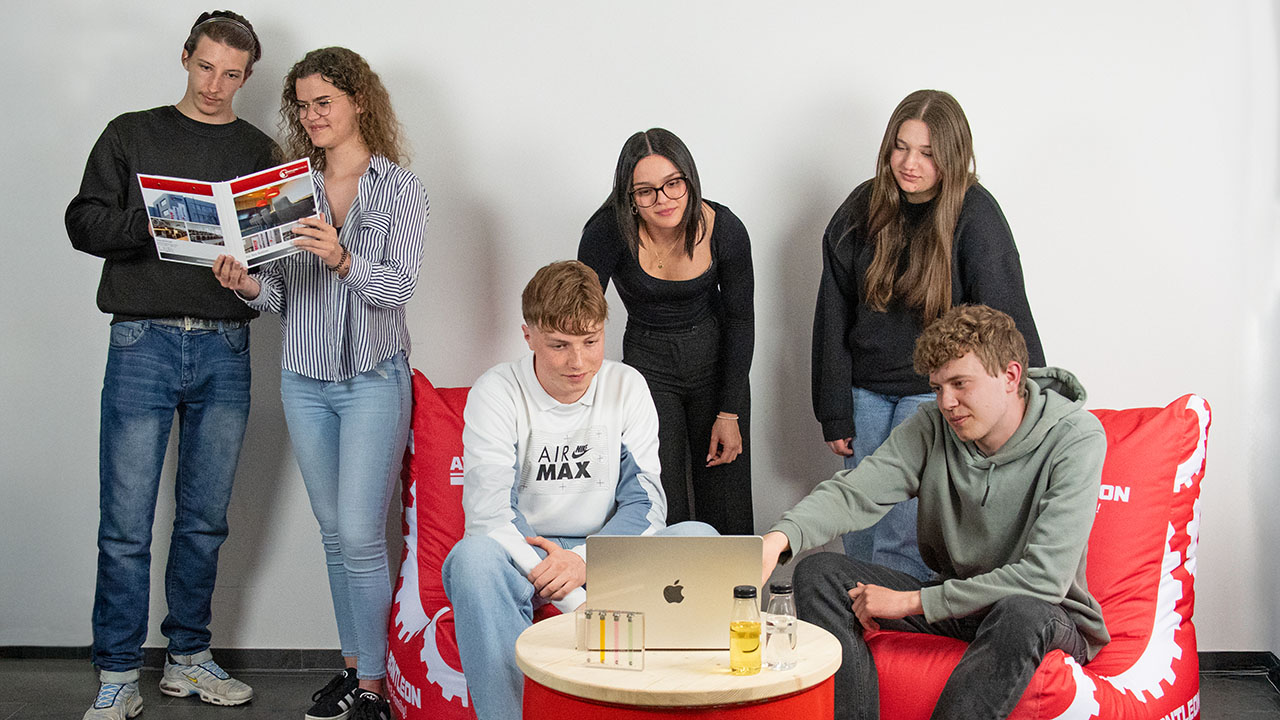 Sechs junge Menschen schauen auf ein Prospekt bzw. auf ein Laptop. 