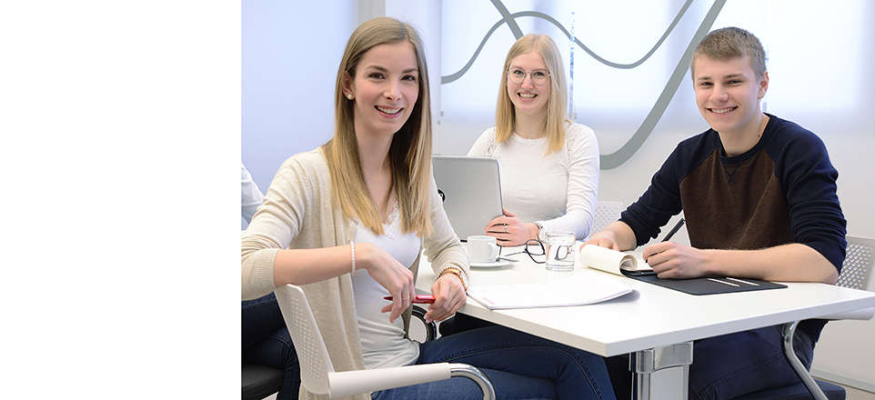 Drei Personen sitzen in einem Büro. 