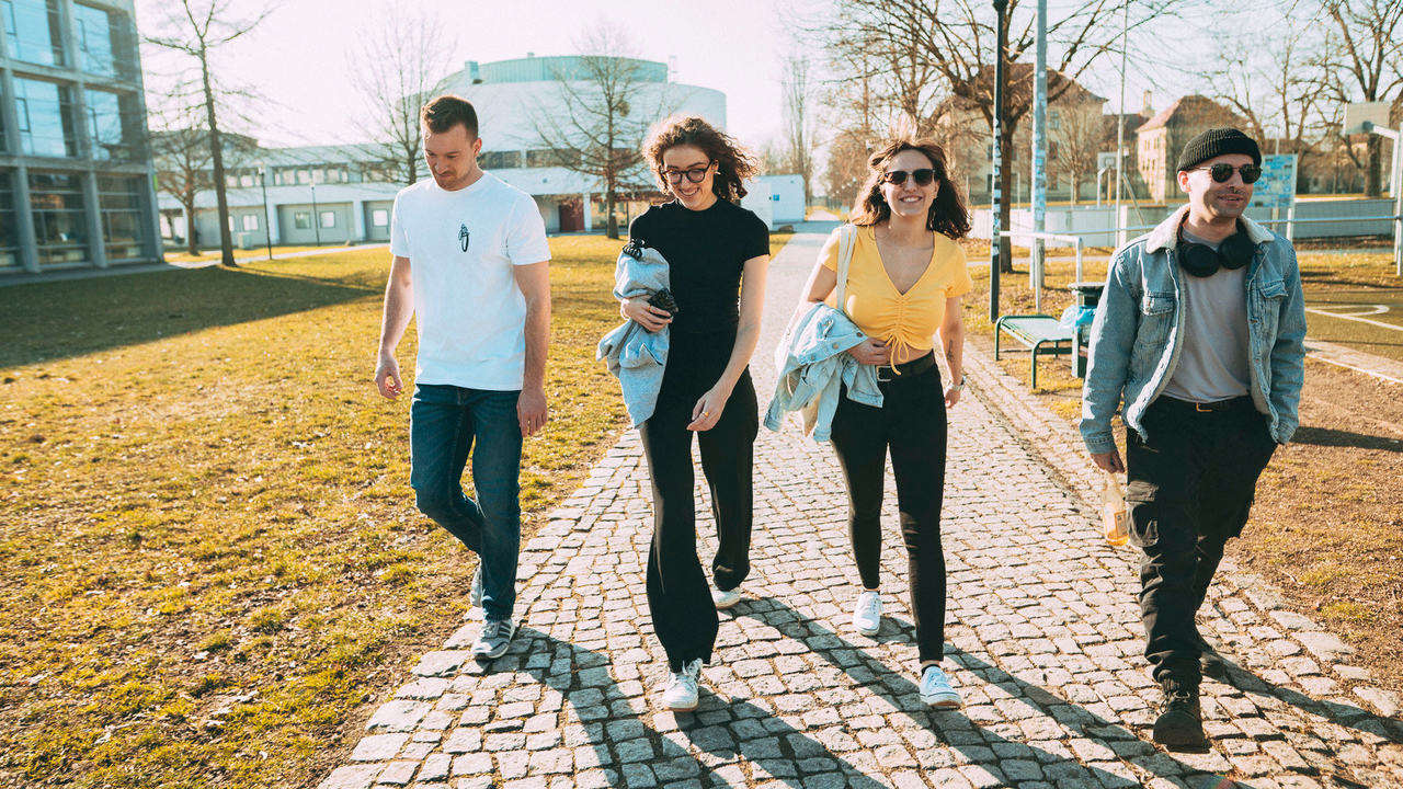 Vier junge Menschen spazieren auf Campusgelände.