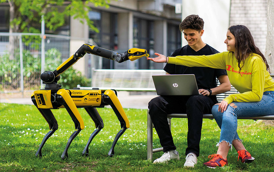 Zwei Studierende sitzen im Park und arbeiten mit einem Roboter