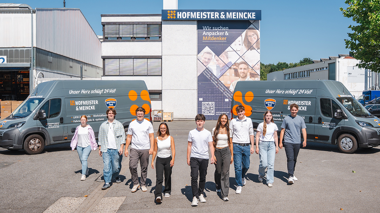 Junge Menschen stehen vor dem Firmengebäude zu einem Gruppenbild. 