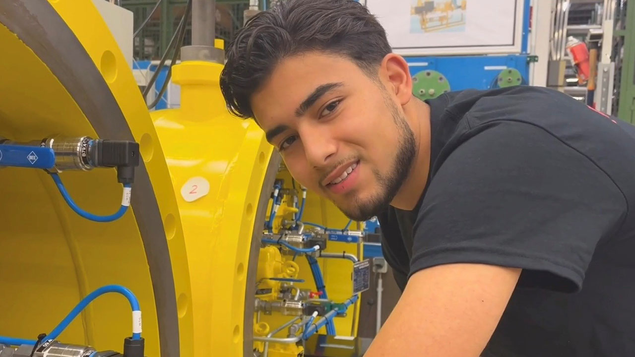 Junger Mensch vor einer Maschine lächelt in die Kamera