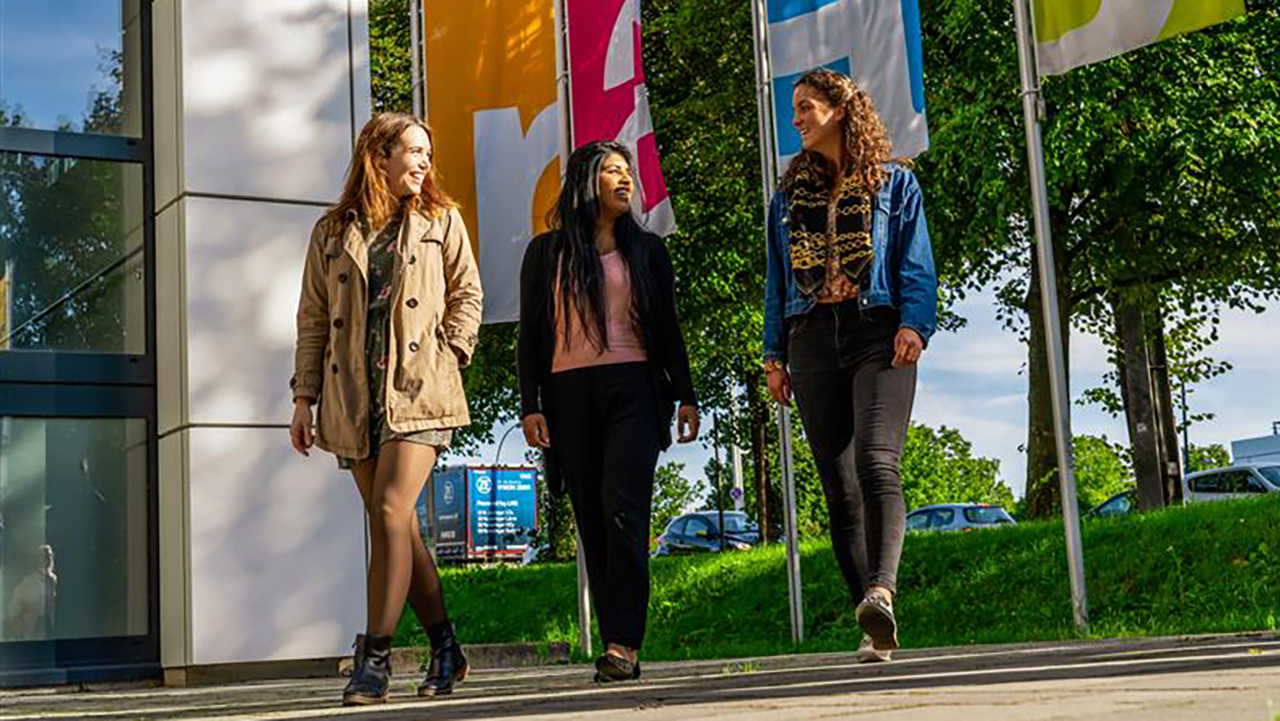 3 Menschen laufen vor der Hochschule und schauen sich an