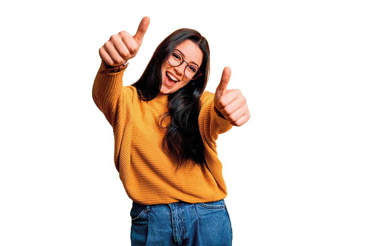 Eine Person mit langen dunklen Haaren lächelt und streckt beide Daumen nach oben.