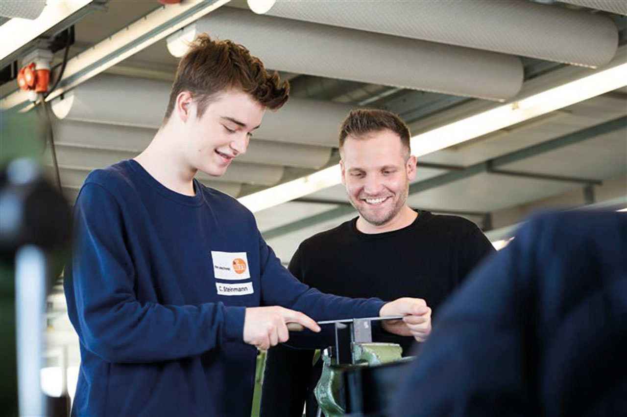 Zwei Personen arbeiten an einem Werkstück und lächeln.