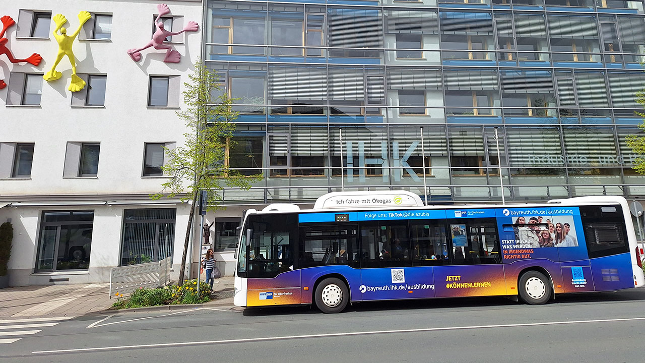 Ein Bus mit Werbung der IHK für Oberfranken Bayreuth fährt vor der Zentrale der IHK entlang. 