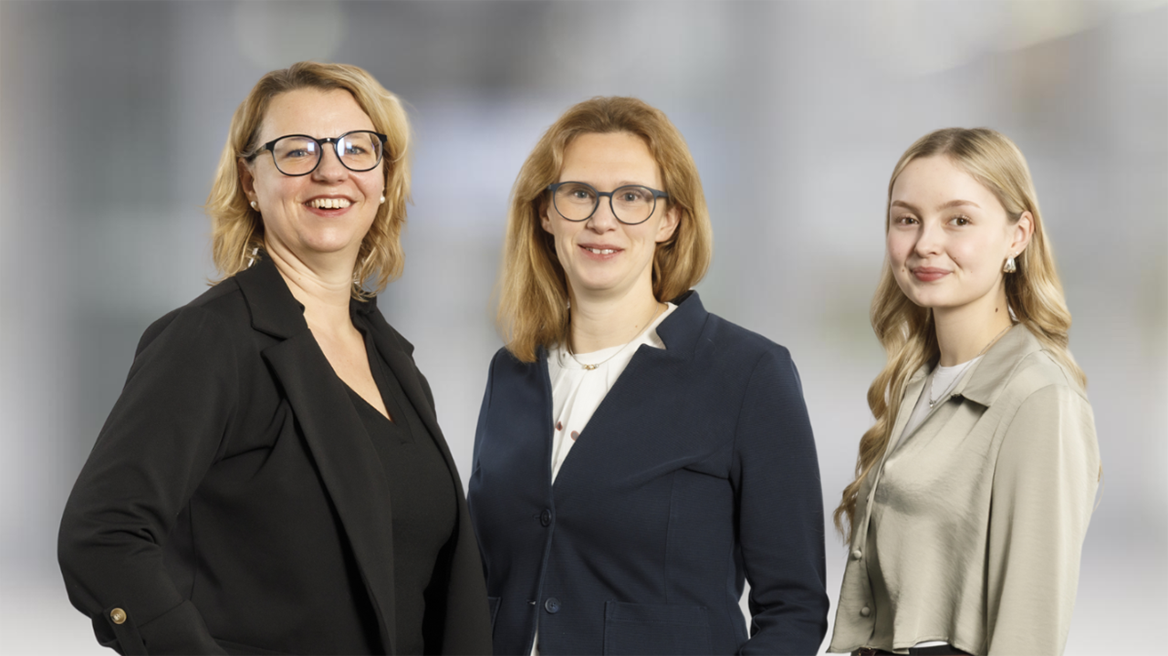 Gruppenbild mit drei Personen vor neutralem grauen Hintergrund