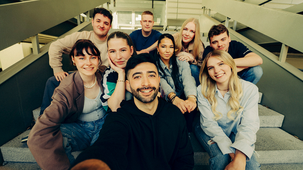 Eine Gruppe junger Menschen sitzt auf einer Treppe und lächelt in die Kamera.