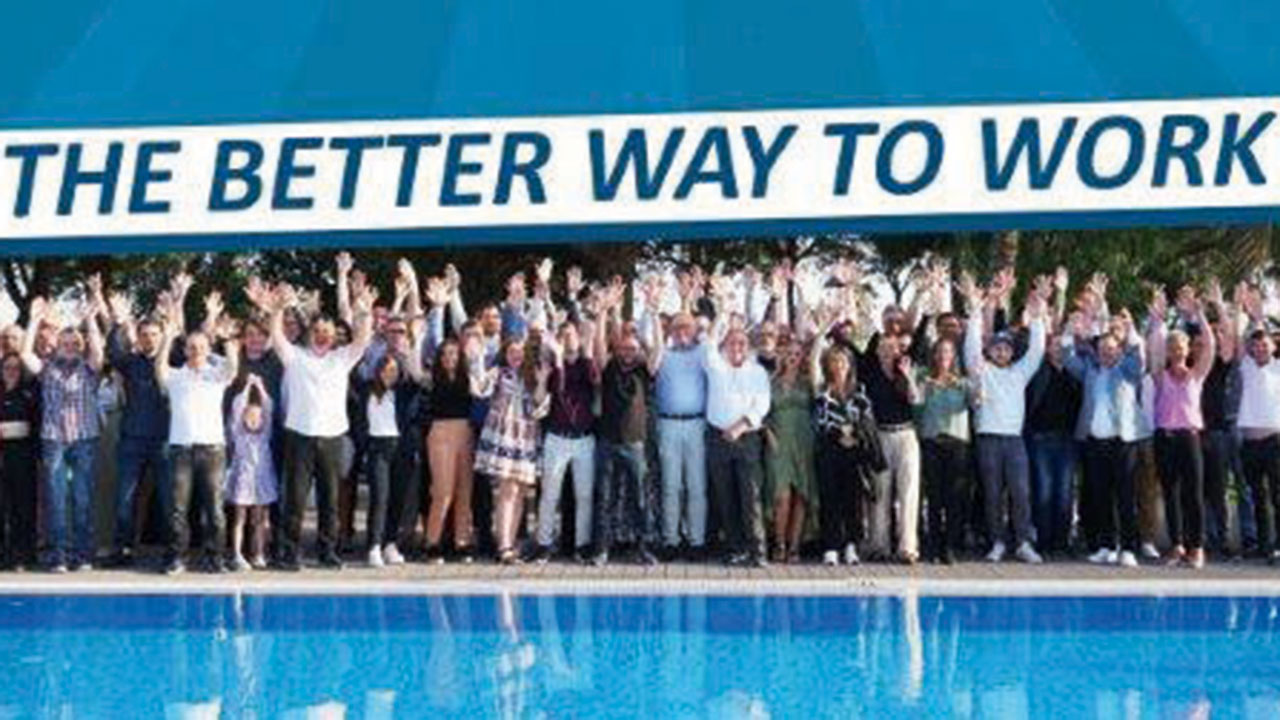 Gruppenfoto am Pool, Banner im Hintergrund mit der Aufschrift: The better way to work