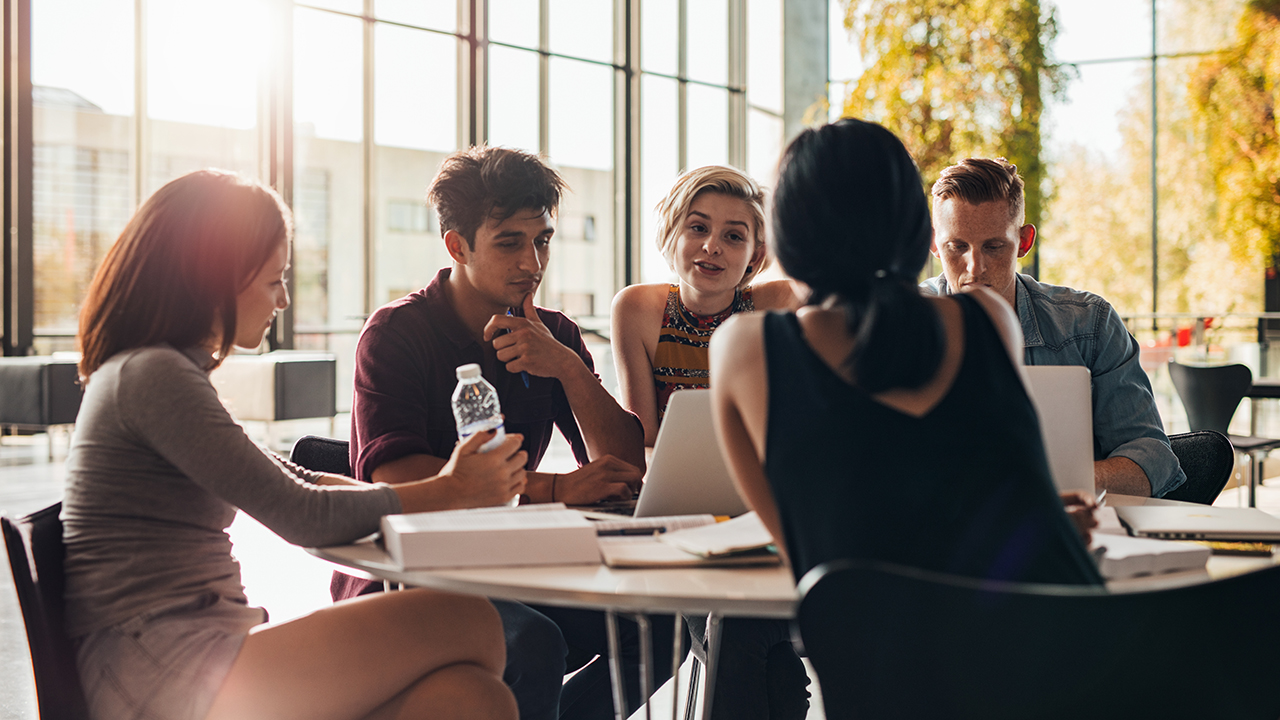 Personen sitzen am Tisch und besprechen etwas.