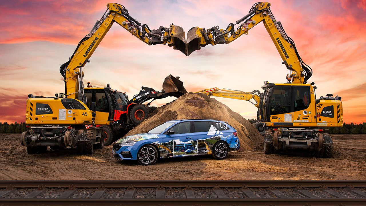Baustelle mit Baggern, davor ein Auto, ganz im Vordergrund Schienen