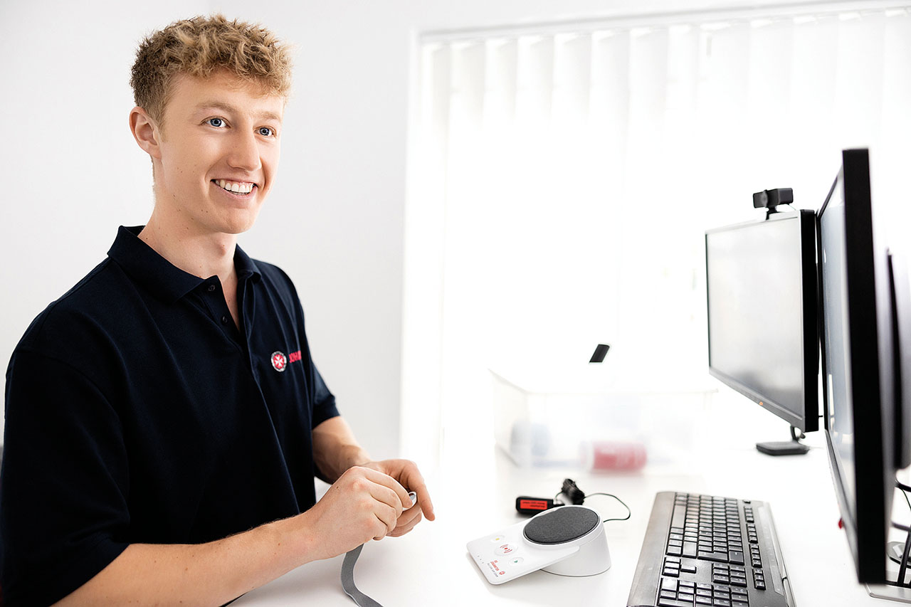 Junge Person sitzt vor einem Computer und lächelt.