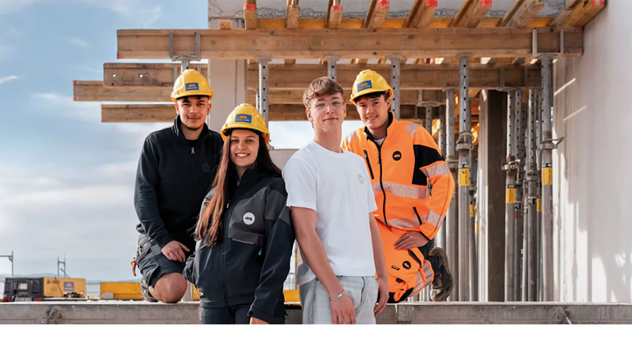 Vier junge Personen in Arbeitsanzügen und gelben Helm