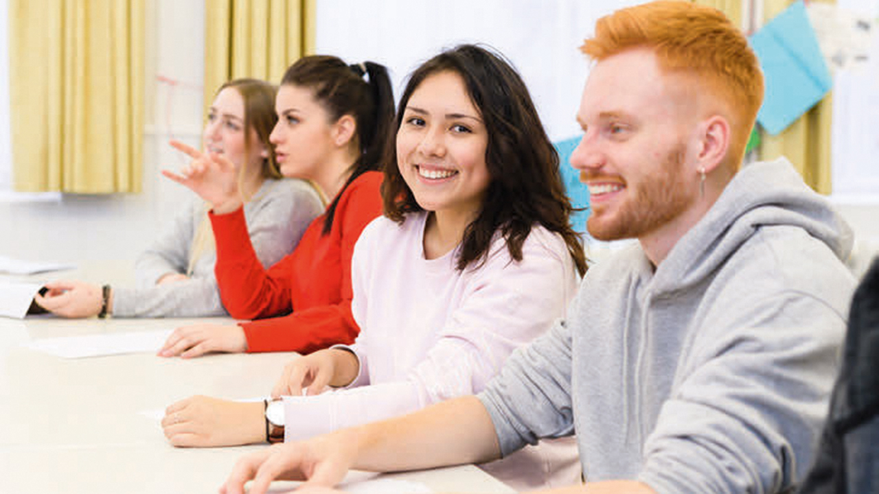 4 Lernende sitzen an einem Tisch nebeneinander in einem Schulungsraum.