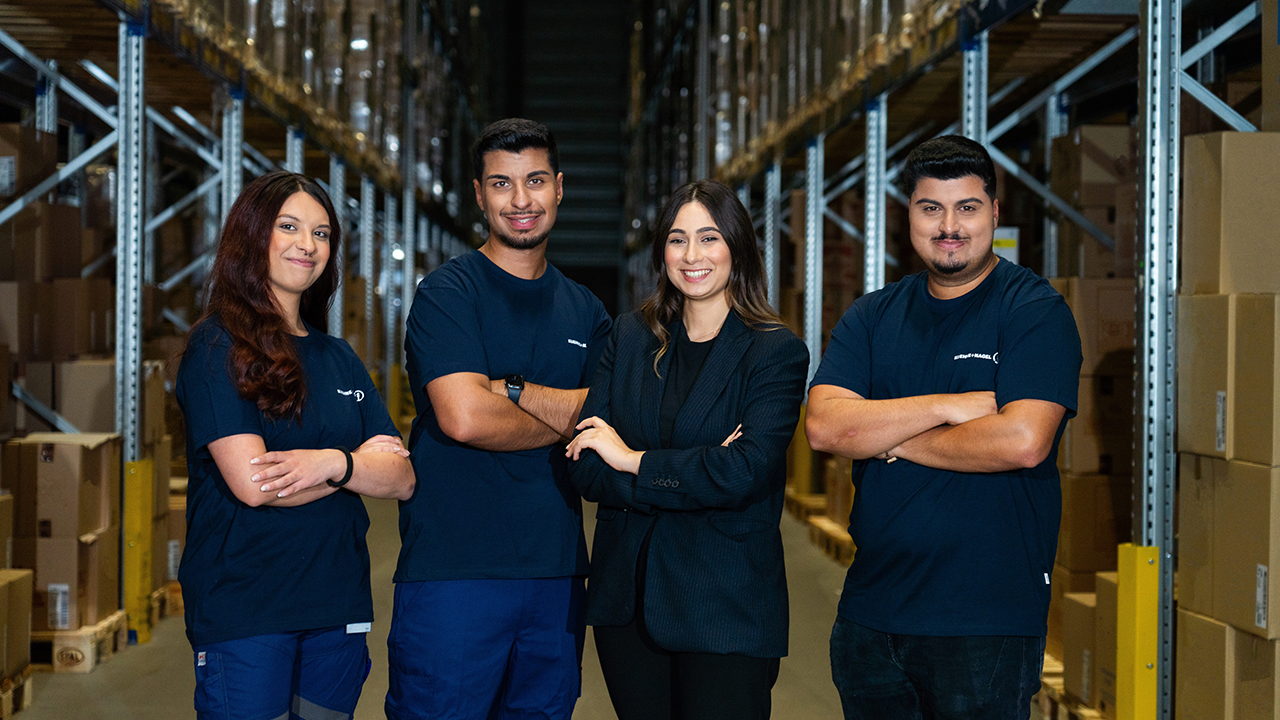 Das Bild zeigt vier Personen die mit verschränkten Armen lächelnd in die Kamera sehen. 