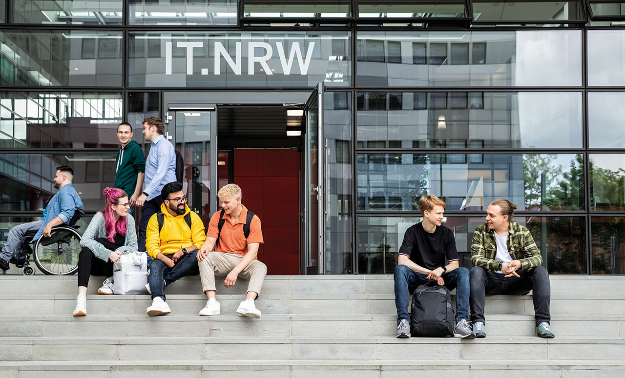 Mehrere junge Menschen sitzen auf den treppen vor dem IT.NRW-Eingang