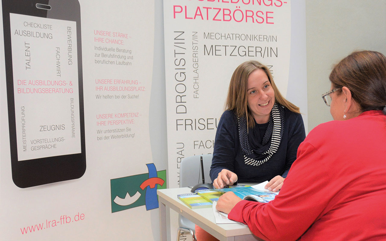 Zwei Personen sitzen an einem Tisch gegenüber. Die eine Person erklärt der anderen Person etwas.