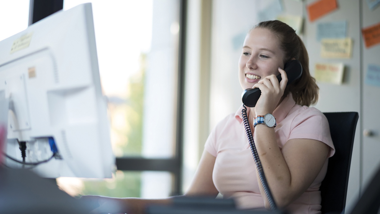 Junge Frau sitzt am Rechner und telefoniert