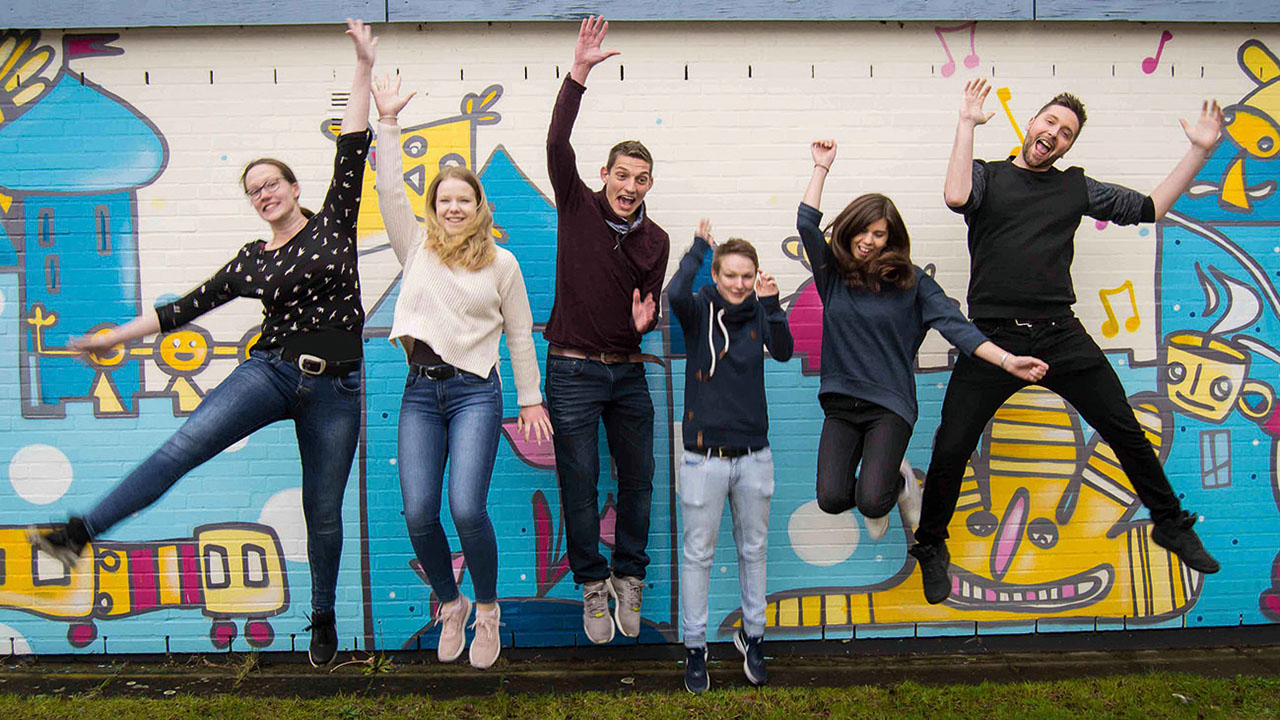 Sechs Menschen springen vor einer bemalten Wand in die Luft