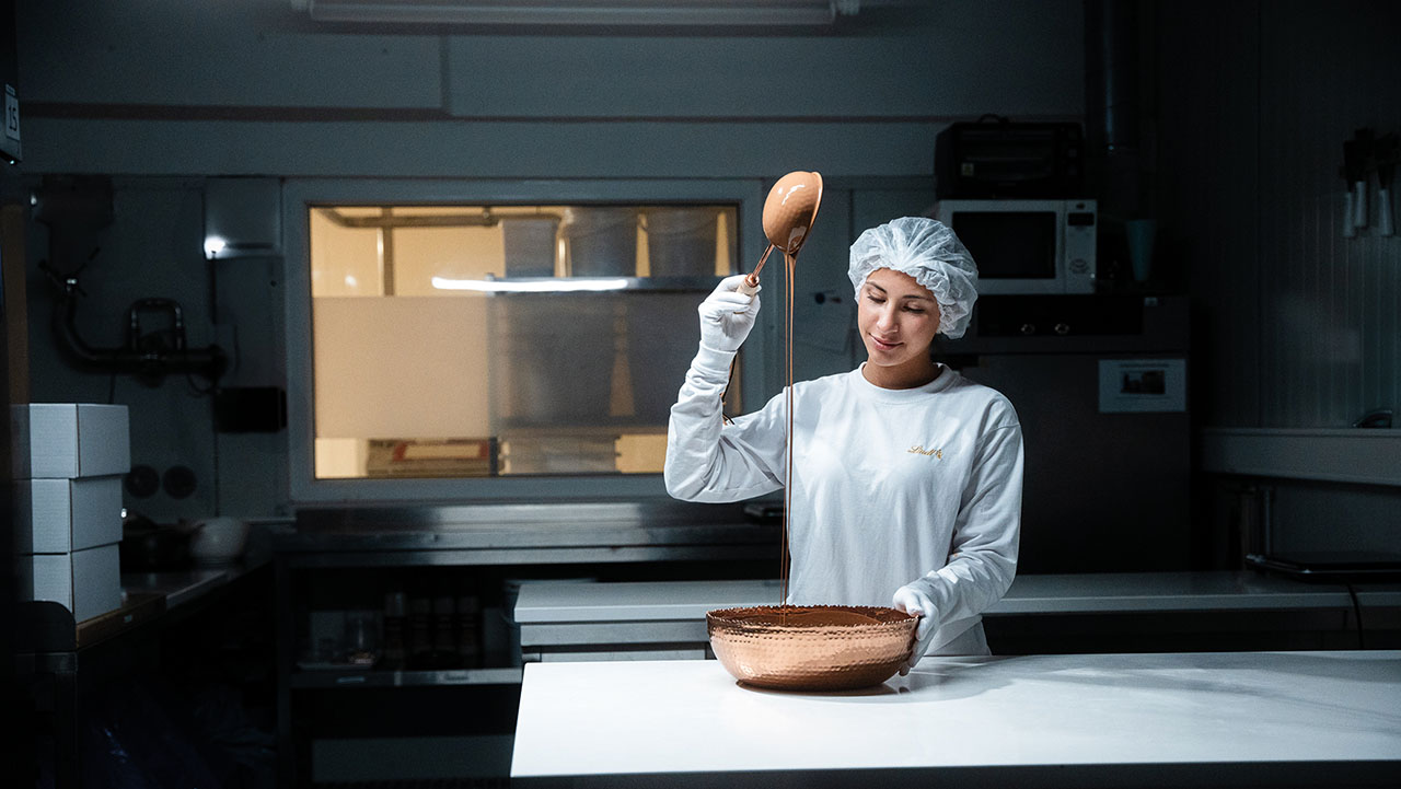 Person in weißer Kleidung hält eine große Kelle voller Schokolade in der Hand.