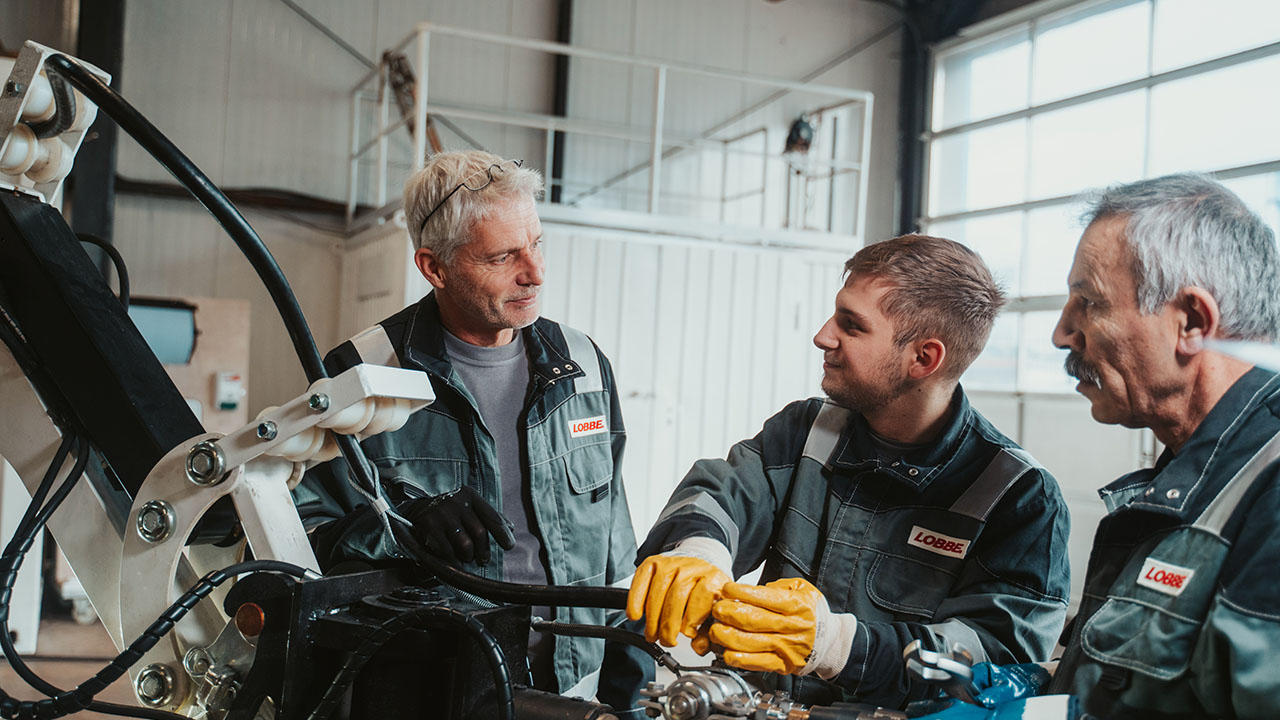 Drei Personen stehen in einer Werkshalle an einer Maschine.
