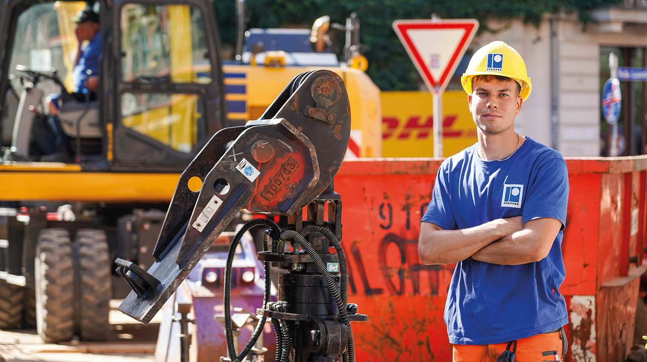 Junger Mitarbeitender in Schutzkleidung auf der Straßenbaustelle