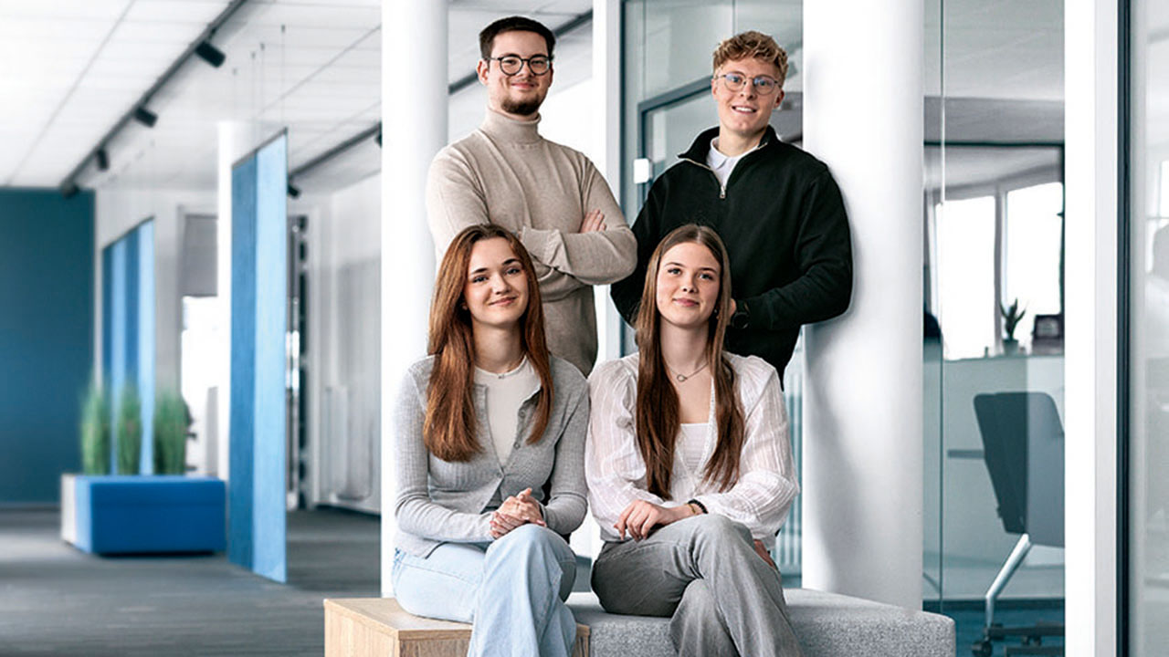 Gruppenfoto im Büro, im Vordergund sitzen zwei junge Menschen, dahinter stehen zwei junge Menschen